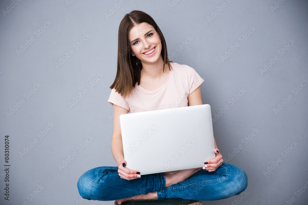 Naklejka premium Happy woman sitting with laptop over gray background