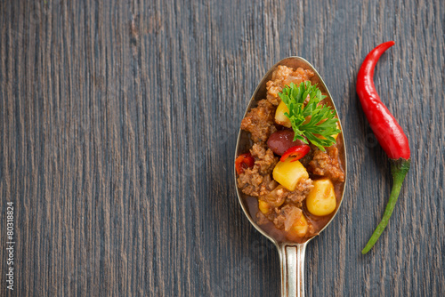 Billede på lærred Mexican dish chili con carne in a spoon on a wooden background