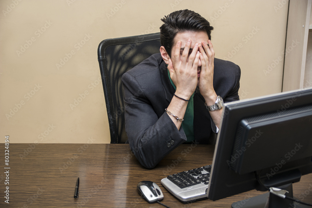 Desperate, worried young businessman sitting at his desk Desperate, worried young businessman sitting at his desk