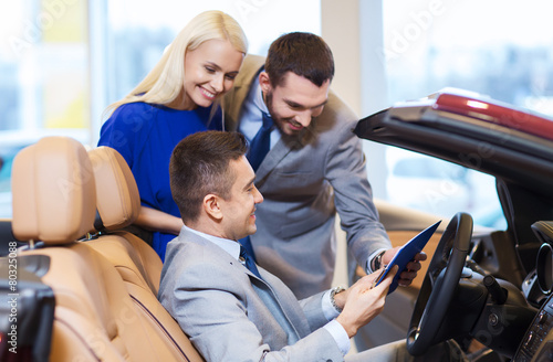 happy couple with car dealer in auto show or salon