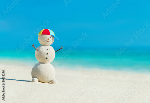 Sandy snowman in rainbow hat on sea beach - happy vacation conce