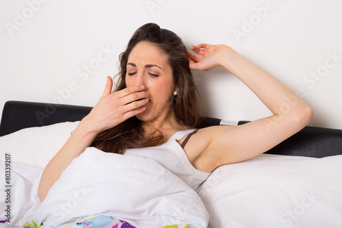tired woman yawning and stretching in bed
