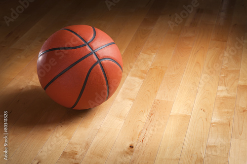 Basketball on hardwood court floor with spot lighting
