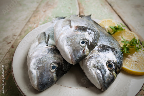 Three fishes (Sparus aurata) on a plate set on wooden table