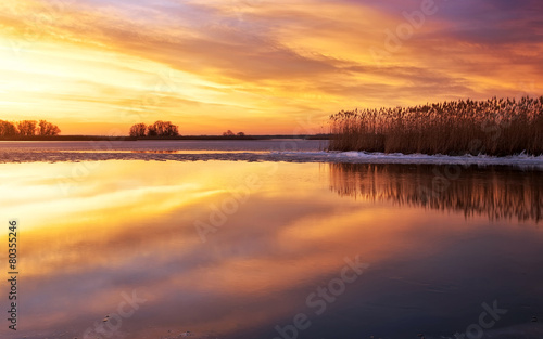 Winter landscape with river, reeds and sunset sky.