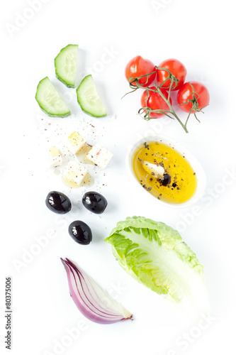 Fototapeta Naklejka Na Ścianę i Meble -  Greek salad recipe ingredients on white from above. Feta cheese, cherry tomatoes, onion, cucumber, olives, lettuce and olive oil.