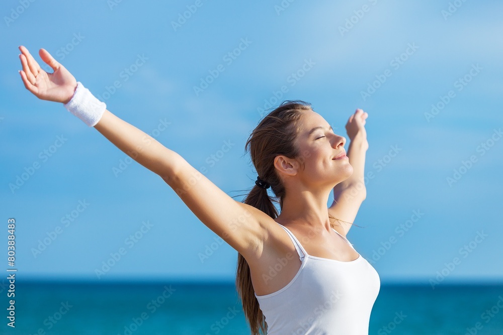 Naklejka premium 20s. Blissful fitness woman raising arms to the sky on beach at