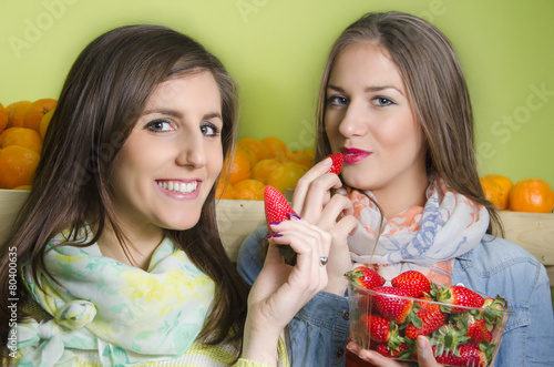 Two beautiful young girls eating strawberries from punnet