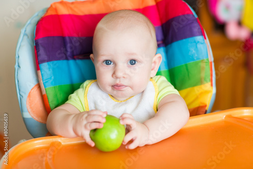 Adorable baby eating apple in high chair