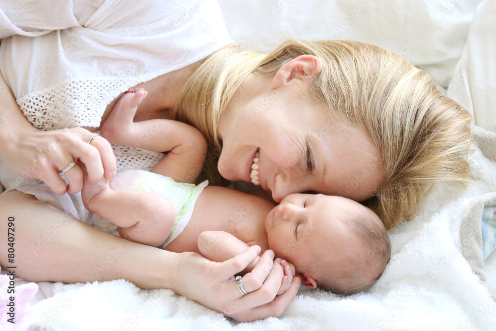Happy Young Mother Snuggling Newborn Baby Daughter in Bed Happy Young Mother Snuggling Newborn Baby Daughter in Bed