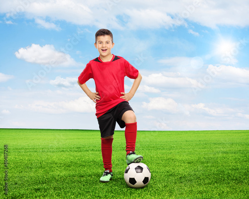 Cheerful youngster standing over a football on field