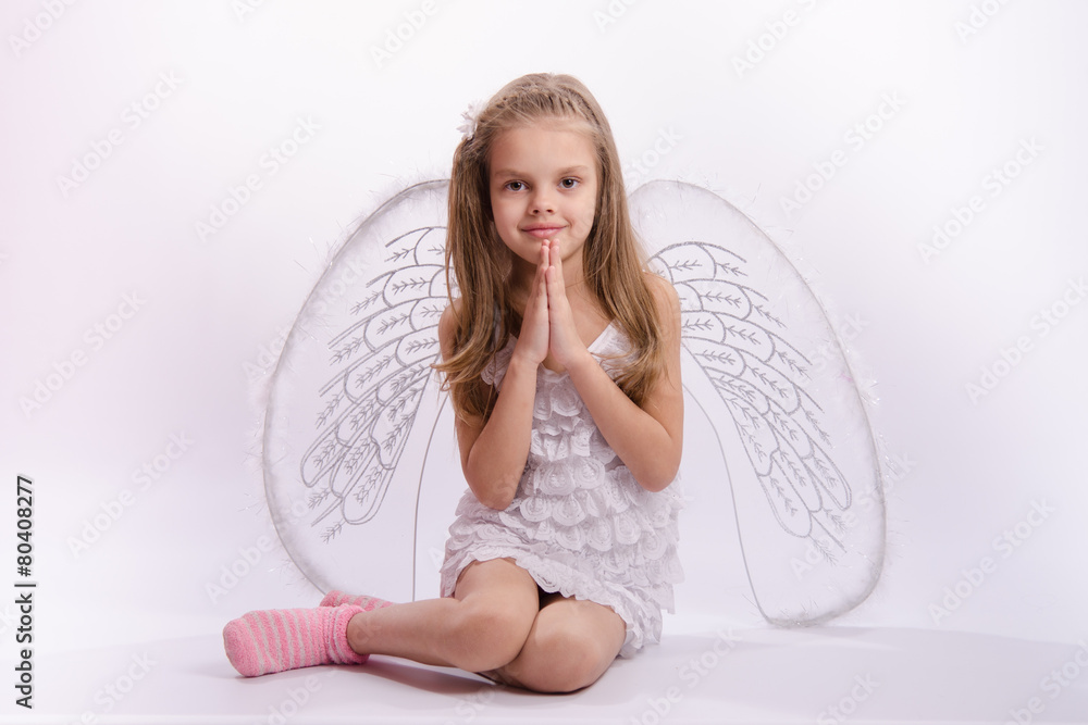 Sitting girl in an angel costume with folded hands Sitting girl in an angel costume with folded hands