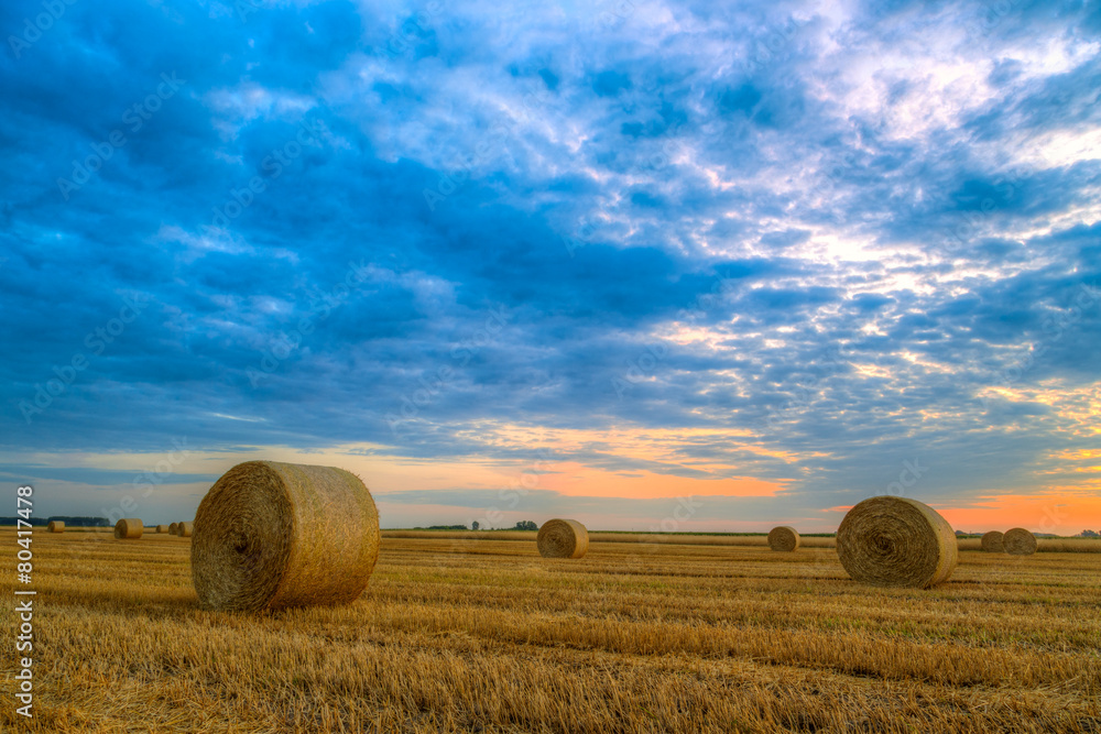 Sunset over farm field with hay bales