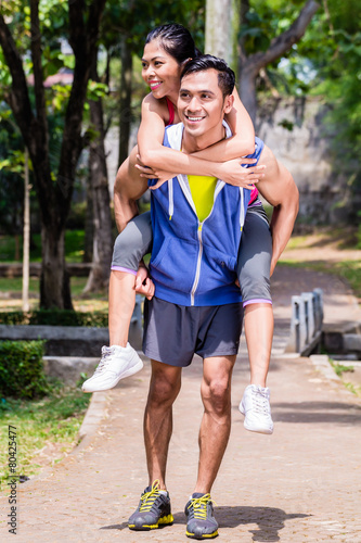 Asian man carrying his girlfriend piggyback for sport