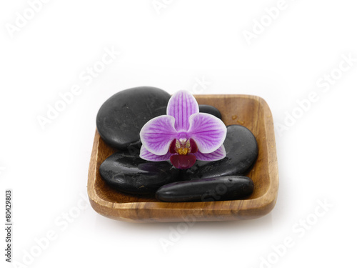 pink orchid with black stones on wooden bowl