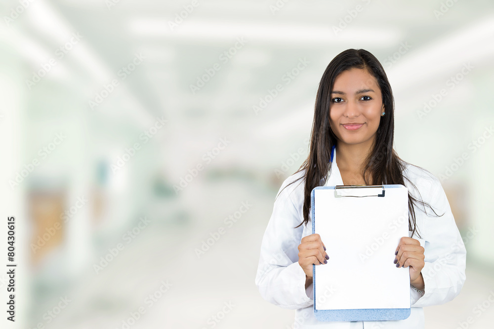 Happy doctor holding clipboard standing in hospital hallway