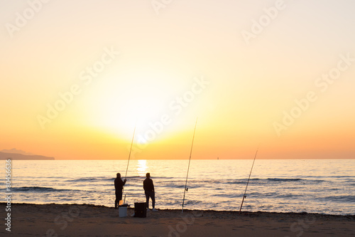 Men fishing on sea beach at sunset
