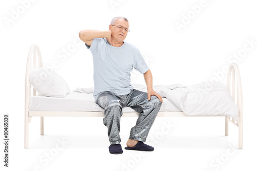 Senior feeling pain in the neck seated on a bed