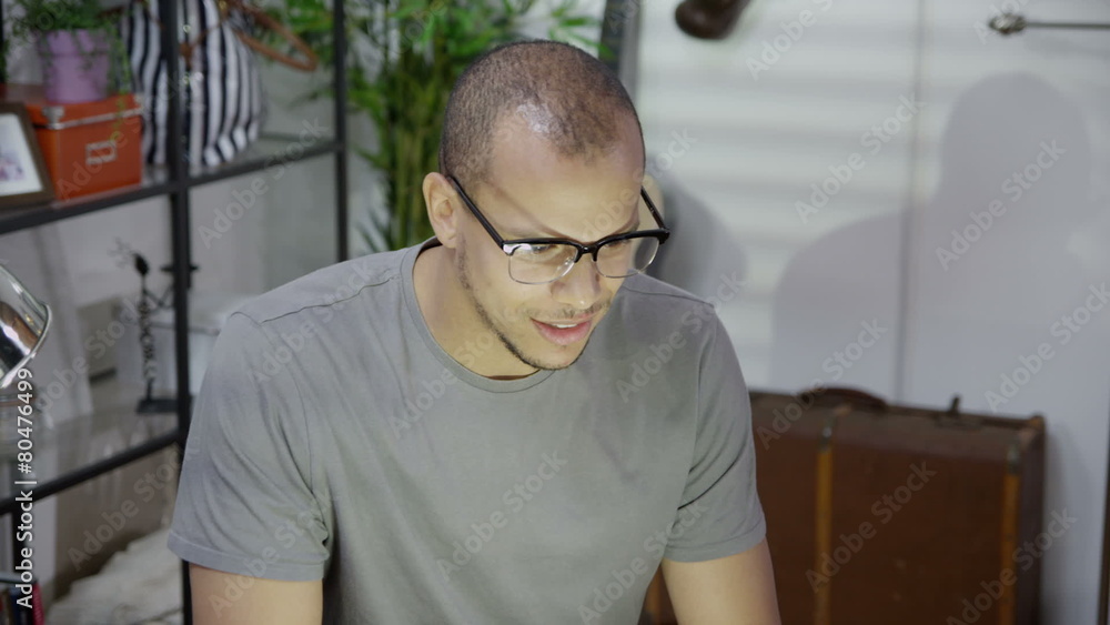 An attractive mixed race man wearing spectacles is surfing the internet at night and drinking coffee. In slow motion. An attractive mixed race man wearing spectacles is surfing the internet at night and drinking coffee. In slow motion.