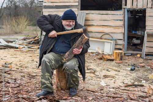 Old farmer is trying to pull out an axe from log