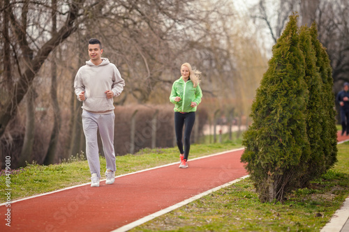 Two young people jogging on running track in the park