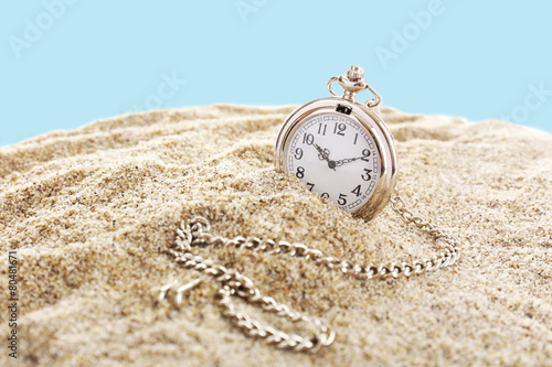 Silver pocket clock on sand on blue background