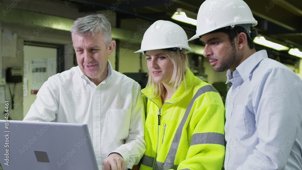 3 workers in a warehouse with a laptop are discussing their work.