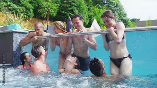 Attractive group of friends enjoy pool party and relaxing in hot tub