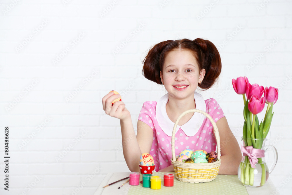 Cute girl decorates Easter eggs, on light background Cute girl decorates Easter eggs, on light background