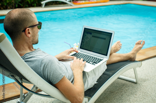 A man working at the computer next to the pool