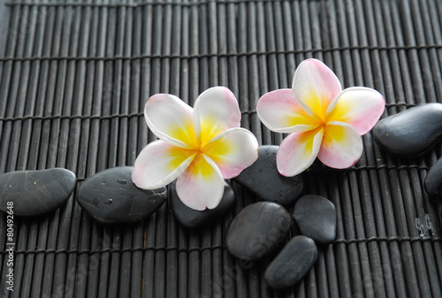 Two pink frangipani flower with pile of stones on bamboo mat