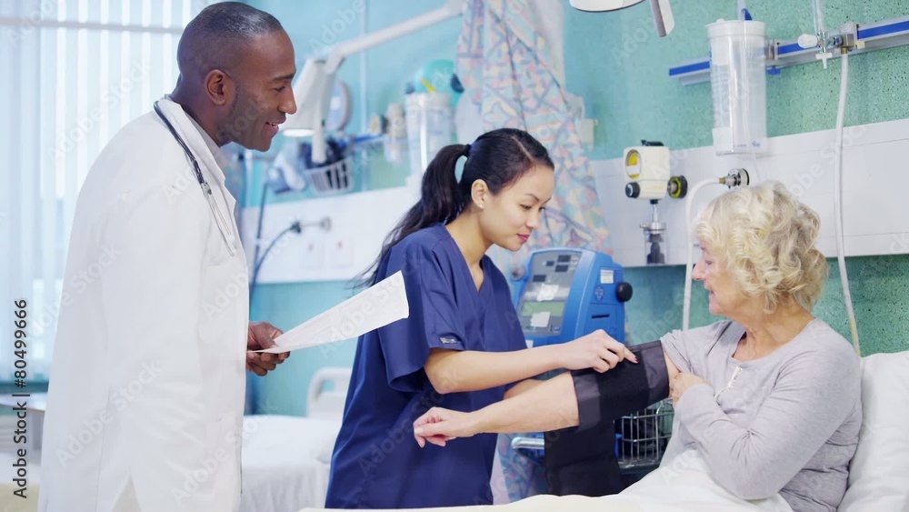 Caring doctor and nurse chatting with an elderly female patient at her bedside Caring doctor and nurse chatting with an elderly female patient at her bedside