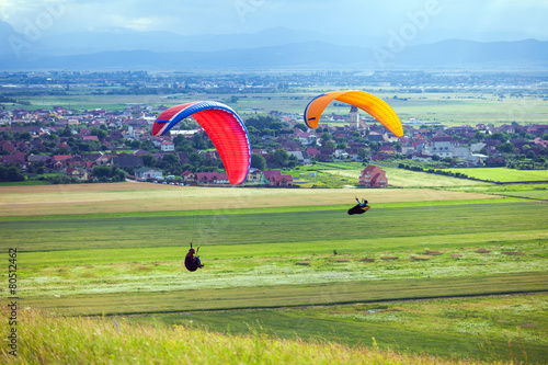 Paragliders flying over green fields