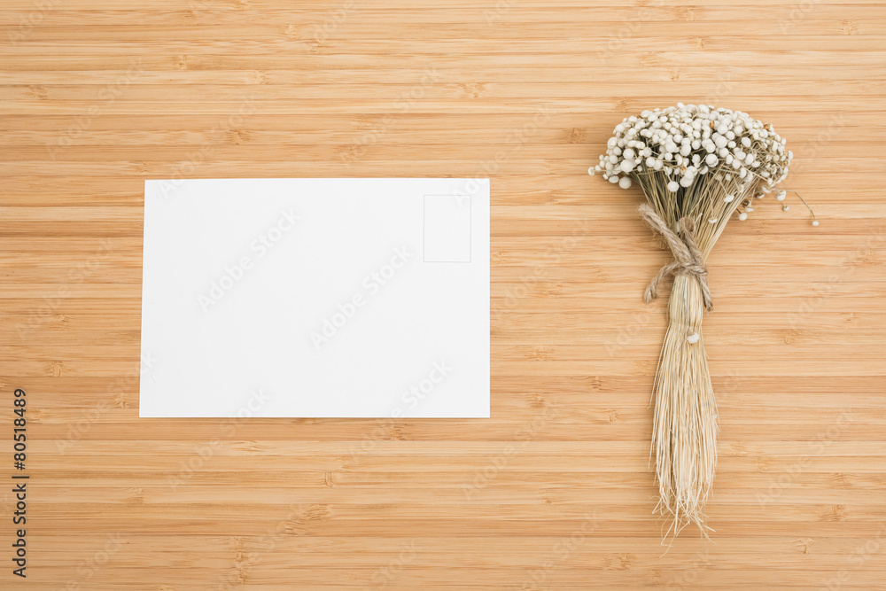 Top view of postcard and dry flower on the wooden background.