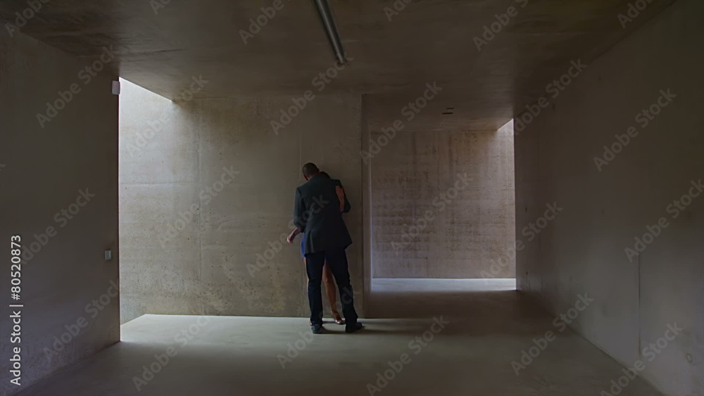 Sexy young couple walking through modern concrete building stop to share a kiss Sexy young couple walking through modern concrete building stop to share a kiss