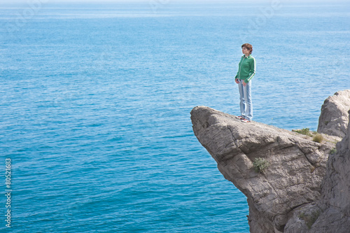 Young slim lonely woman standing at the edge of mountain cliff a