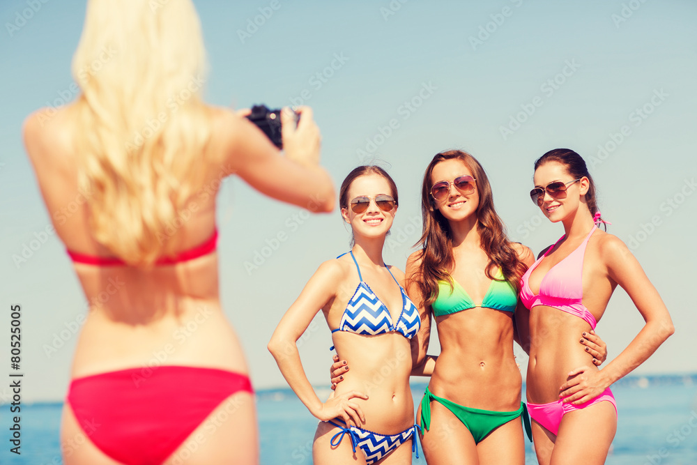 group of smiling women photographing on beach