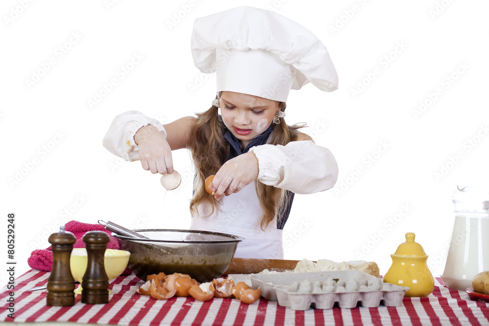Little cook girl in a white apron breaks eggs in a deep dish Little cook girl in a white apron breaks eggs in a deep dish
