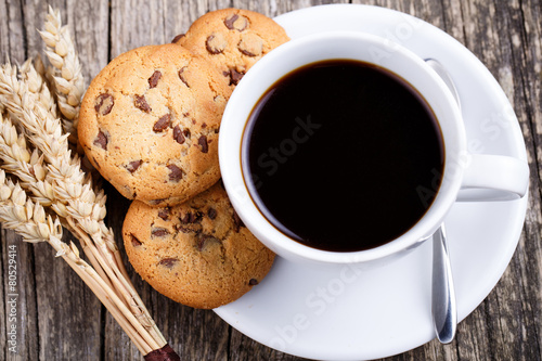Cup of coffee with cookies and wheat on a table.