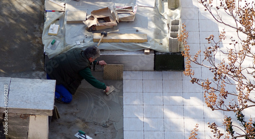 Un carreleur posant des dalles sur une terrasse