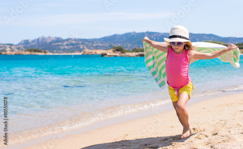 Little happy girl running on beach with towel