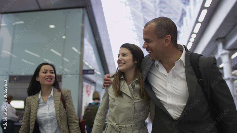 Young professional group chat as they walk through a busy railway station
