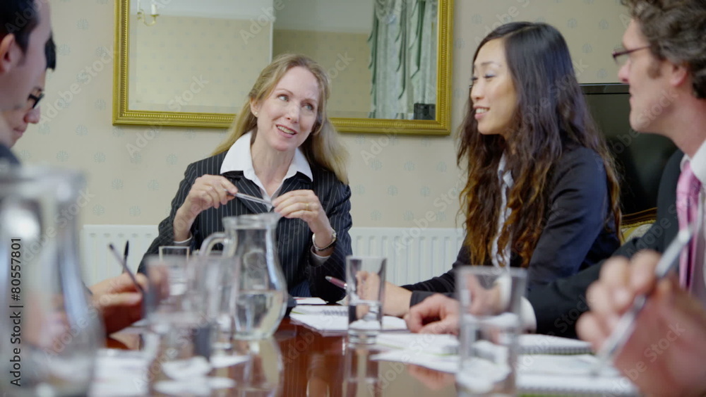 Diverse team of professionals in a boardroom meeting looking over the figures Diverse team of professionals in a boardroom meeting looking over the figures