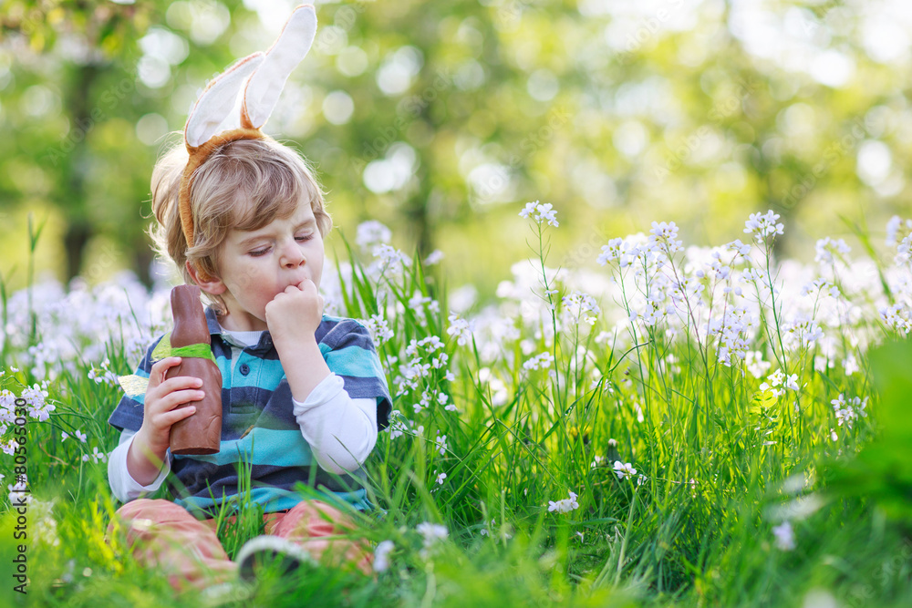 Cute happy little boy wearing Easter bunny ears and eating choco Cute happy little boy wearing Easter bunny ears and eating choco