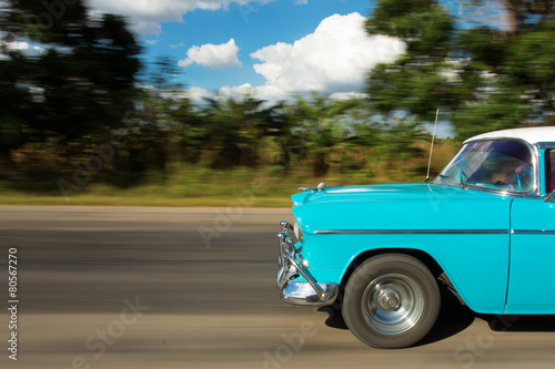 Old classic car on the road in Cuba with white clouds and blue s