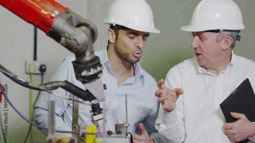 Mature male factory manager explains to younger man how the machinery works Mature male factory manager explains to younger man how the machinery works