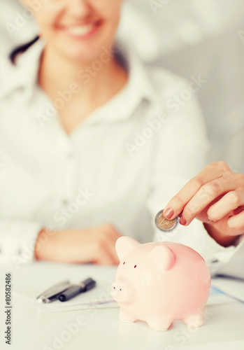 woman hand putting coin into small piggy bank photo