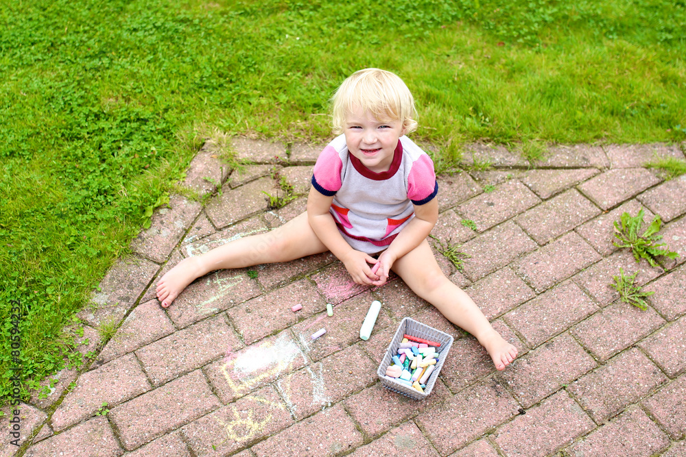 Little girl drawing with chalk at the backyard of the house