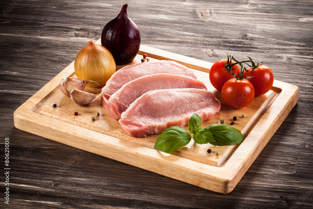 Raw pork chops on cutting board and vegetables Raw pork chops on cutting board and vegetables