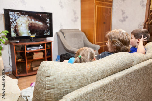 People watching tv at home, mother and her two kids: girl, boy